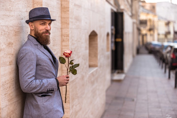 handsome stylish man with a beard and a hat with a flower in his hands