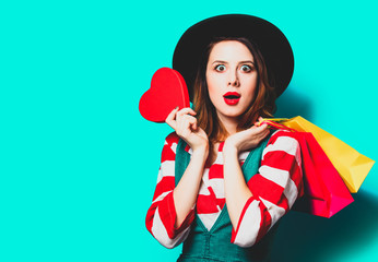 Portrait of young surprised red-haired white european woman in hat and red striped shirt with heart...