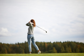 Young woman in activewear holding golf club after hitting ball while standing on the field