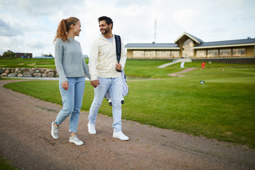 Young amorous couple in casualwear holding by hand while moving down road after playing golf