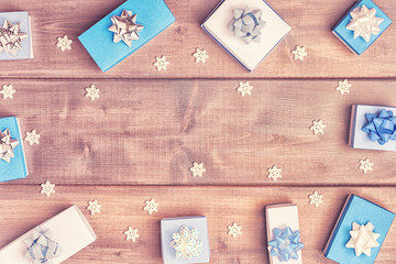 Small blue and white boxes with bows and snowflakes are laid out in a circle on a wooden background. Christmas composition with copy space. Festive layout.