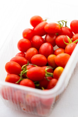 Fresh organic cherry tomatoes, inside plastic package, on white background.