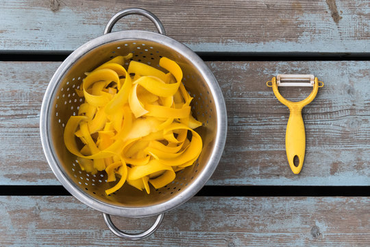 Yellow Zucchini Ribbons In A Steel Bowl And A Yellow Vegetable Knife On Faded Wooden Boards. Top View, Horizontal Slits.