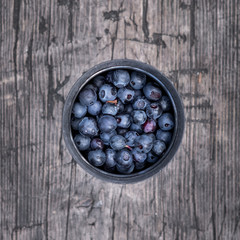 A cup filled with fresh blueberries on a wooden surface.