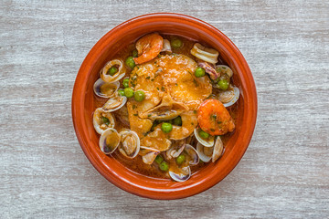 Hake in sauce in a clay pot on a wooden table.