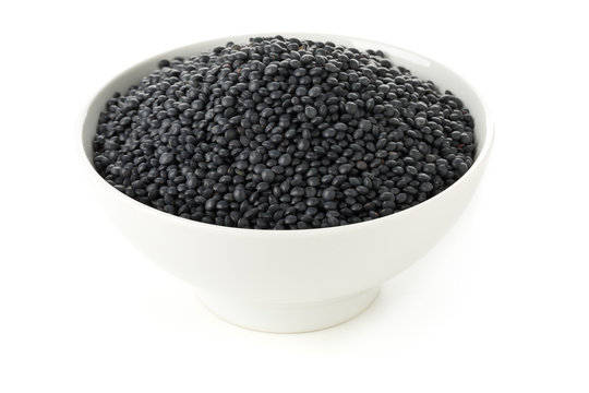 Heap of black organic beluga lentils in white bowl on white