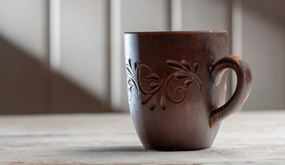 Clay mug with patterns on a white wooden table, in the morning sun rays