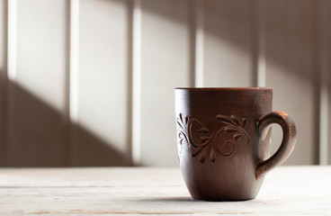 Clay mug with patterns on a white wooden table, in the morning sun rays