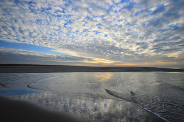 Zach&oacute;d Słońca na plaży pod częściowo zachmurzonym niebem.