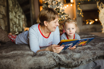 Grandma and granddaughter have fun together reading a book on the bed . Family Christmas concept.