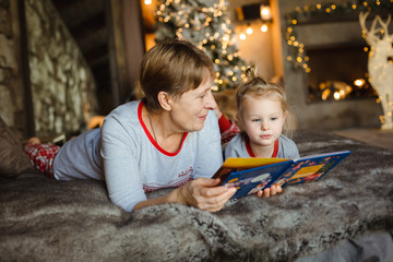 Grandma and granddaughter have fun together reading a book on the bed . Family Christmas concept.