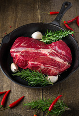 cast iron pan with raw ribeye steak on wooden background.