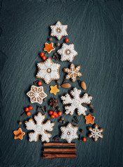 Obraz na płótnie Canvas Gingerbread, nuts, spices, dried orange peel create a Christmas tree on a dark stone background for your design. Holiday, celebration and cooking concept. new year and christmas postcard.