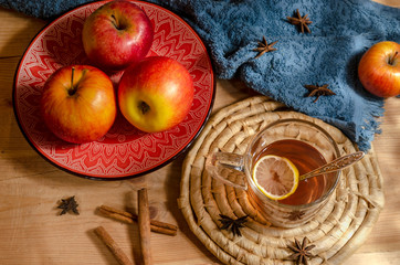 Apples in a ceramic red plate, a glass of mulled wine, sweets on a wooden table.