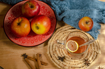 Apples in a ceramic red plate, a glass of mulled wine, sweets on a wooden table.