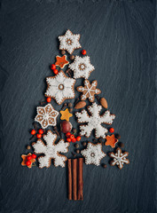 Gingerbread, nuts, spices, dried orange peel create a Christmas tree on a dark stone background for your design. Holiday, celebration and cooking concept. new year and christmas postcard.