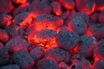 Coals smolder and glow. Residual flame from smoldering coals in cinder, closeup view. Flicker of...