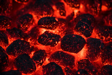 Coals smolder and glow. Residual flame from smoldering coals in cinder, closeup view. Flicker of burning coals at night.