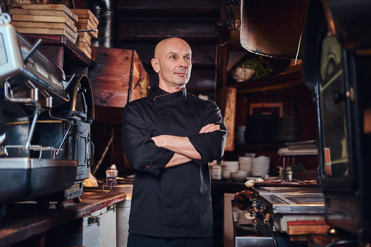 Confident chef posing with his arms crossed and looking away in a restaurant kitchen.