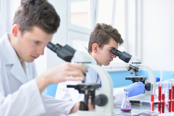 Two Young male scientists looking through a microscope in a laboratory doing research, microbiological analysis, medicine.