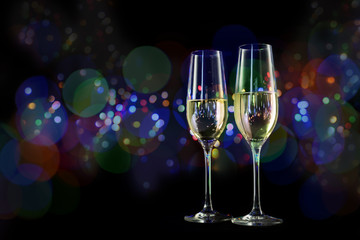 two champagne glasses in front of a dark background with colorful blurred bokeh lights, new year and party concept with copy space