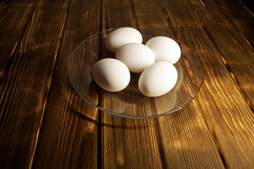 White chicken eggs in a transparent plate on a rustic wooden table. Natural