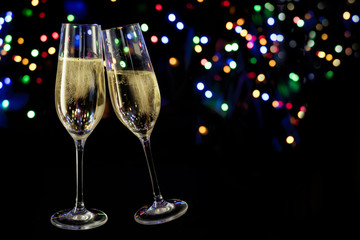 two champagne glasses toast against a dark background with colorful bokeh lights, new year and party concept with copy space