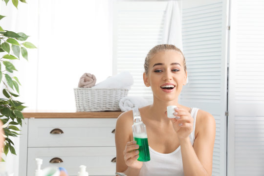 Woman holding bottle and cap with mouthwash in bathroom. Teeth care