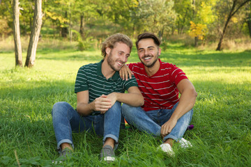 Fototapeta premium Portrait of happy gay couple sitting on grass in park