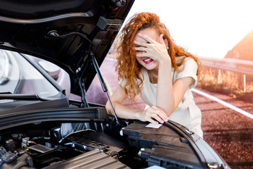 Fototapeta na wymiar Redhead girl standing in front of a broken car on the road