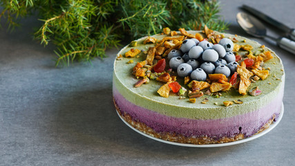 Vegan raw cake with blueberry, cherry, matcha tea, orange,  cashew cream, coconut butter and coconut milk, and base made of almonds, dates  and  dried apricots, oat flakes, lyophilisated berry