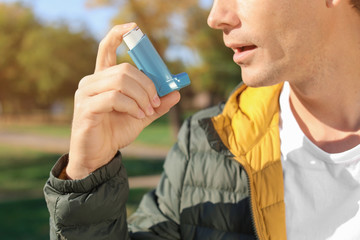 Man using asthma inhaler outdoors. Health care
