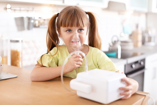 Little girl using asthma machine at table in kitchen