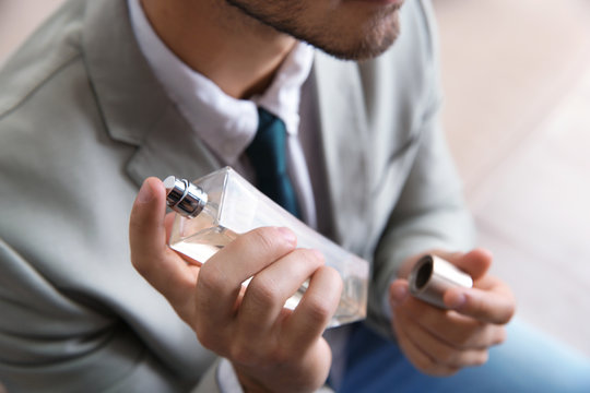 Businessman applying perfume on blurred background, closeup