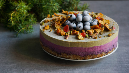 Vegan raw cheesecake with blueberry, cherry, matcha tea, orange,  cashew cream, coconut butter and coconut milk, and base made of almonds, dates  and  dried apricots, oat flakes, lyophilisated berry