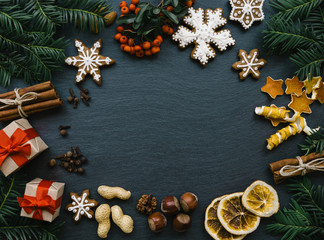 Frame with fir branches, Gingerbread cookies and Christmas decorations on dark stone background. Top view.