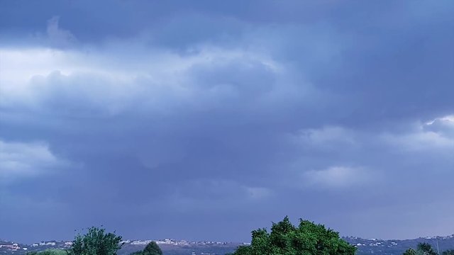 Thunder strikes as large storm clouds move across Northcliff Johannesburg Gauteng South Africa. Wind blows and moves the trees in the foreground - A storm is coming. Camera pans left along horizon.