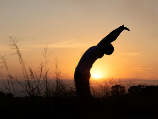 Silhouette of the sunset with the back of the man stretching the body.