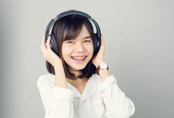 Asian girl in white casual dress listening to music from black headphones. In a comfortable and good mood, on a gray background gives a soft light.