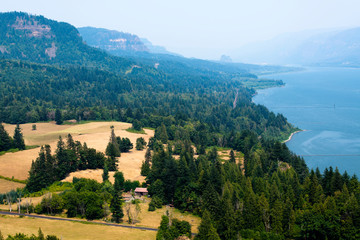 Fototapeta na wymiar The mountainous coast of the winding Columbia River with trees and meadow with house in Columbia River Gorge