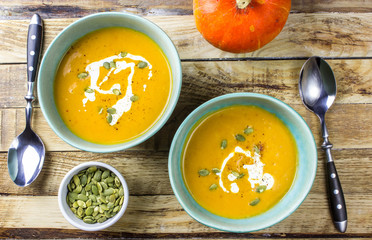 Roasted pumpkin and carrot soup with cream and pumpkin seeds on wooden background. Top view. Copy space