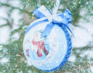 Christmas ball with a snowman on a branch in a winter forest