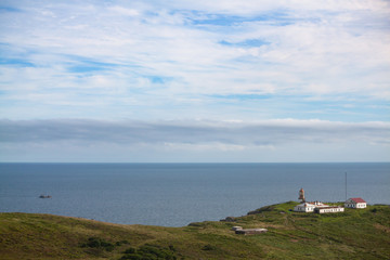 Fototapeta na wymiar Lighthouse Povorotny against blue sky with white clouds. Russia, Far East, coast of Sea of Japan