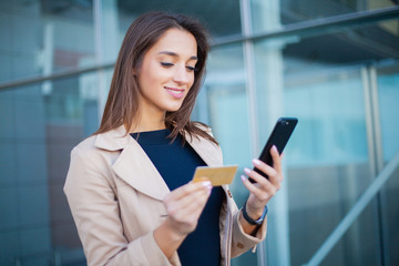 Low Angle Of Pleased Girl Standing at the Airport Hall. He is Using Gold Credit card and Cellphone For Paying