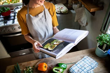 Fototapeten Glückliche Frau, die ein Kochbuch in der Küche liest © Rawpixel.com