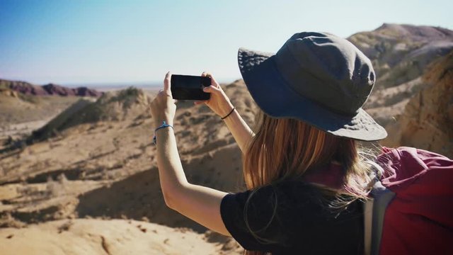 Young traveler hipster female making picture by smartphone sitting in middle of endless desert with mountains rock with a beautiful view of blue sky in vacations or holidays travel to stunning Nature