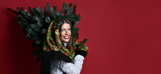 Happy Russian style woman with scarf hold Christmas  tree on her shoulders happy laughing 
