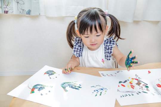 手の平に絵具を塗り遊ぶ幼い女の子。育児、子育て、教育、知育イメージ