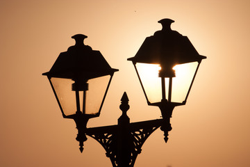 the sun shines through the street lamp