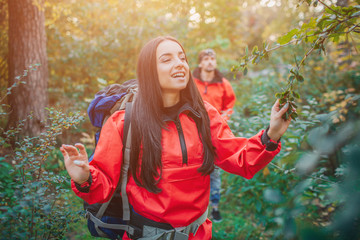 Positive picture of young woman enjoying. She keeps eyes closed and smile. Guy walks behind her. They travel. People are in forest.